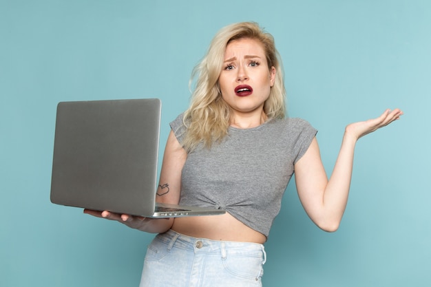 female in grey shirt and bright blue jeans using a laptop