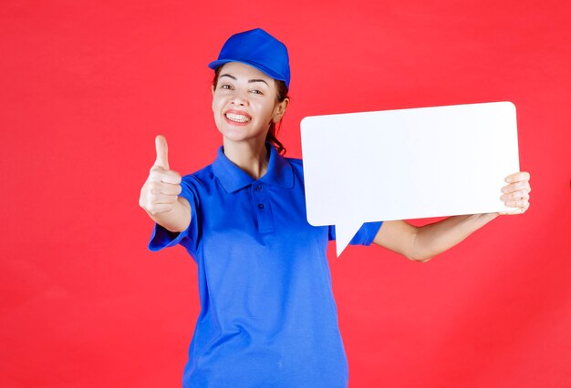 Female guide in blue uniform holding a white rectangular info board and showing enjoyment sign. 