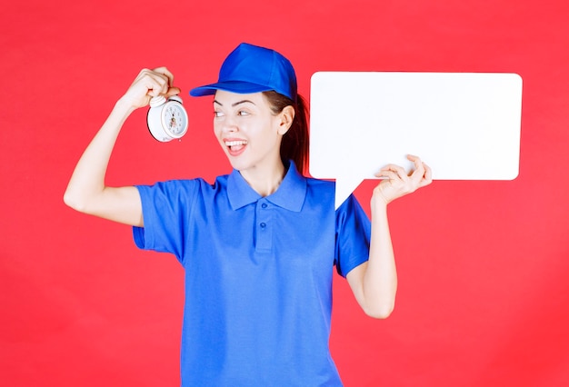 Female guide in blue uniform holding a white rectangular info board with an alarm clock . 