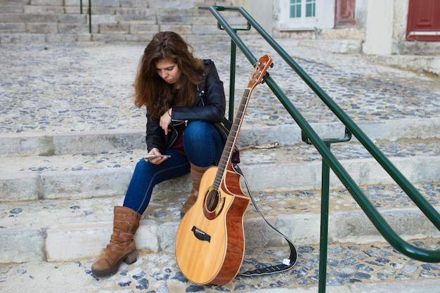 Female Guitarist Using Smartphone on City Stairs