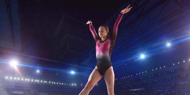 Foto gratuita ginnasta femminile che fa un trucco complicato sulla trave di equilibrio di ginnastica in un'arena professionale