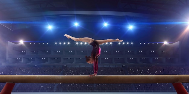 Ginnasta femminile che fa un trucco complicato sulla trave di equilibrio di ginnastica in un'arena professionale