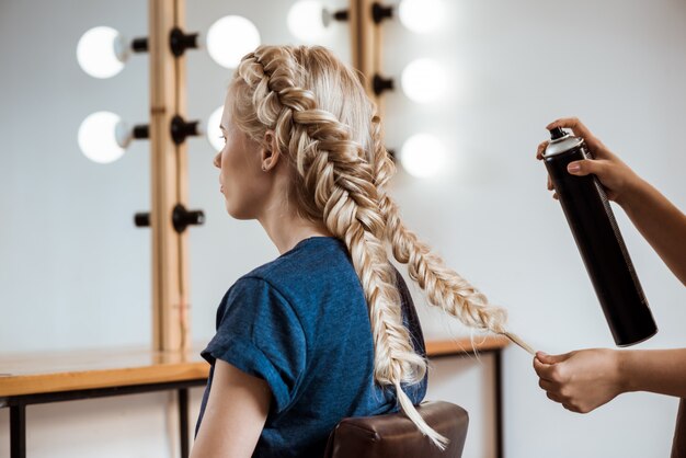 Female hairdresser making hairstyle to blonde woman in beauty salon