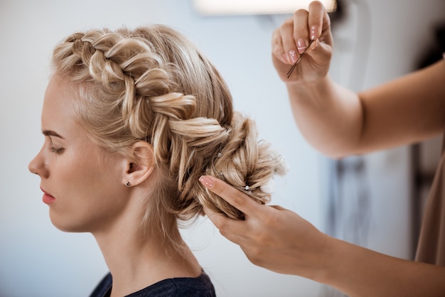 Женский парикмахер делает прическу блондинке в салоне красоты