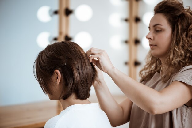 Female hairdresser making hairstyle to brunette woman in beauty salon