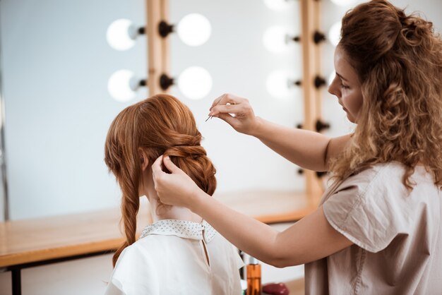 Female hairdresser making hairstyle to redhead woman in beauty salon