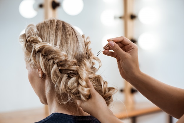 Женский парикмахер делает прическу блондинке в салоне красоты