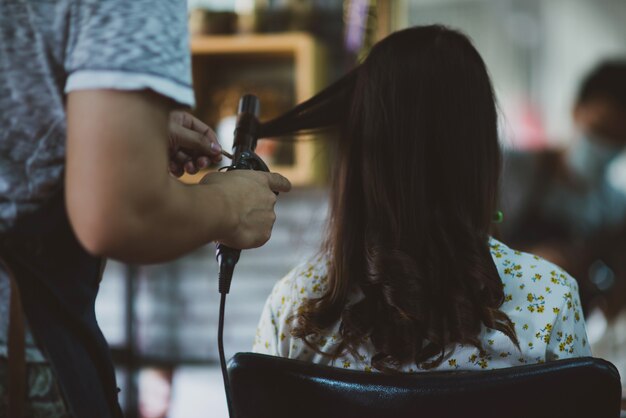 female hairdresser standing, face makeup and making hairstyle to cute lovely young woman in beauty salon