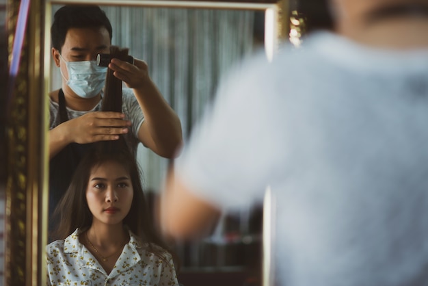 female hairdresser standing, face makeup and making hairstyle to cute lovely young woman in beauty salon