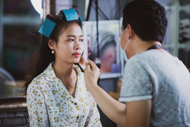立っている女性の美容師、顔メイクと美容院でかわいい素敵な若い女性に髪型を作る