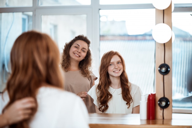 Female hairdresser and woman smiling, looking in mirror in beauty salon