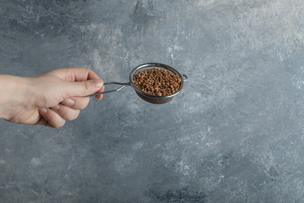 Female hand filtering raw buckwheat with strainer