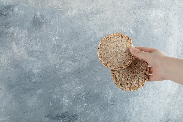 Free photo female hand holding airy crispbread on marble surface