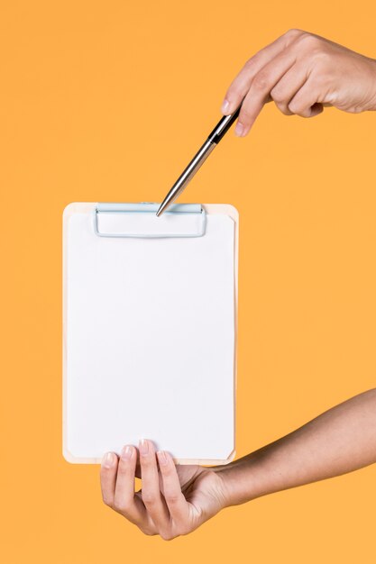 Female hand holding blank clipboard and pen over yellow background