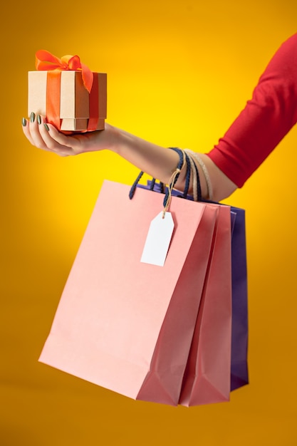 Female hand holding bright shopping bags on yellow