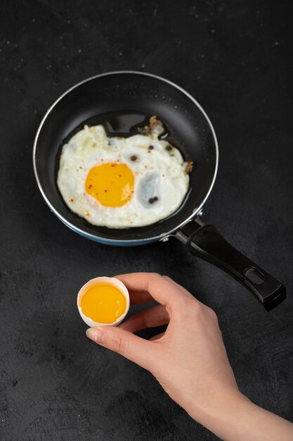 Female hand holding broken egg on black surface.