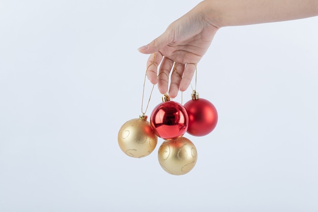 Female hand holding Christmas baubles on white surface