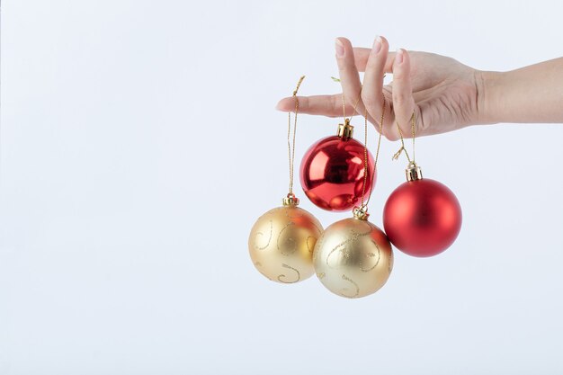 Female hand holding Christmas baubles on white surface
