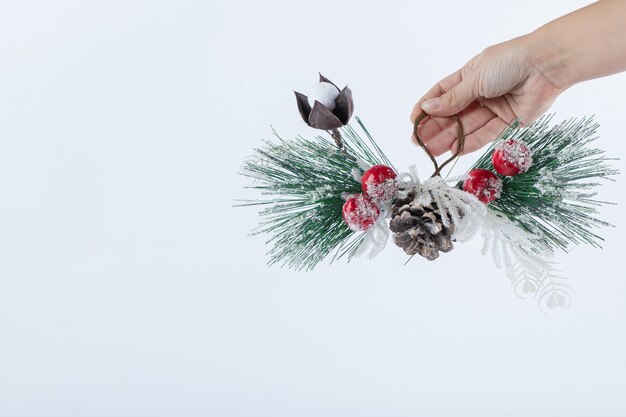 Female hand holding Christmas pinecone on white surface