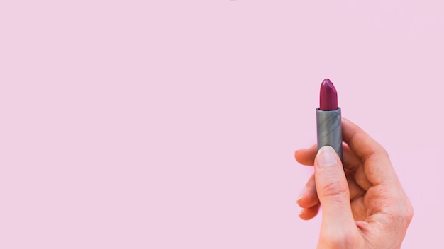 Female hand holding dark shade lipstick on pink background