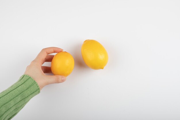Female hand holding fresh yellow lemon on white.