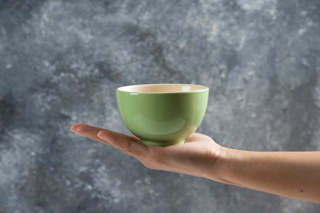 Female hand holding a green bowl on gray.