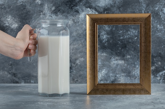 Female hand holding jug of milk on marble.