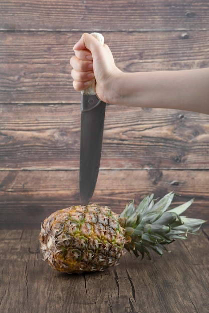 木製の背景にパイナップルを切るための女性の手持ちナイフ