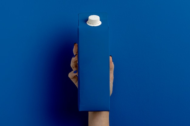 Female hand holding milk container on classic blue 