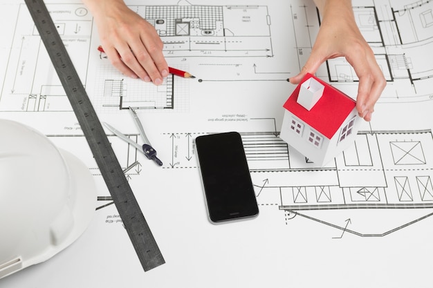 Female hand holding model house over blueprint at office