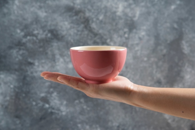 Female hand holding a pink bowl on gray.