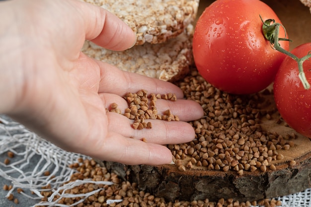 Female hand holding raw buckwheat from wooden piece