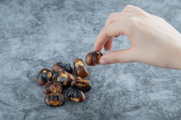 Female hand holding roasted chestnut on marble surface