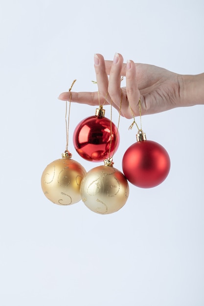 Female hand holding shiny Christmas baubles on white surface