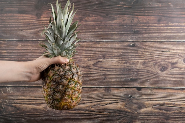 Female hand holding single fresh pineapple on wooden background