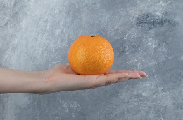 Female hand holding single orange on marble table. 