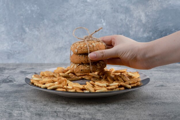 Female hand holding stack of oatmeal cookies on marble background.