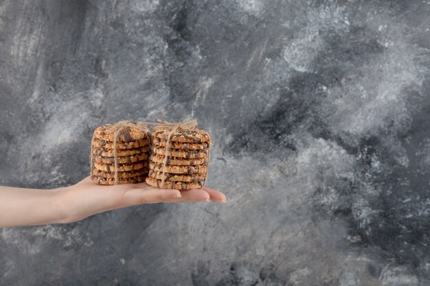 Female hand holding stack of oatmeal cookies on marble background.