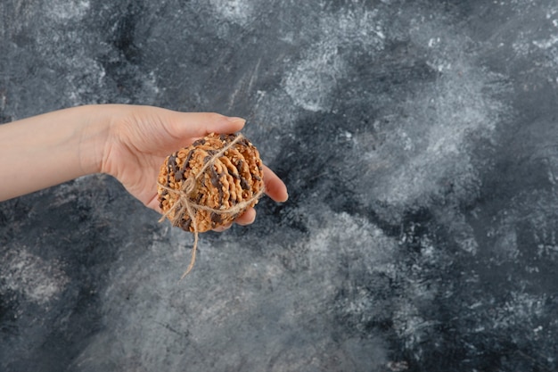 Female hand holding stack of oatmeal cookies on marble background.