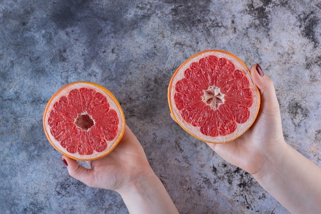 Female hand holding two grapefruit slices on grey.