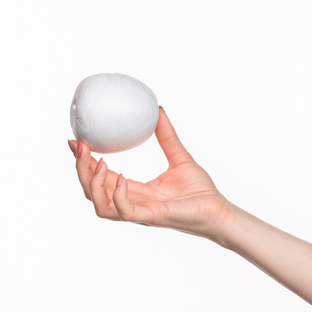 The female hand holding white blank styrofoam oval against the white background.