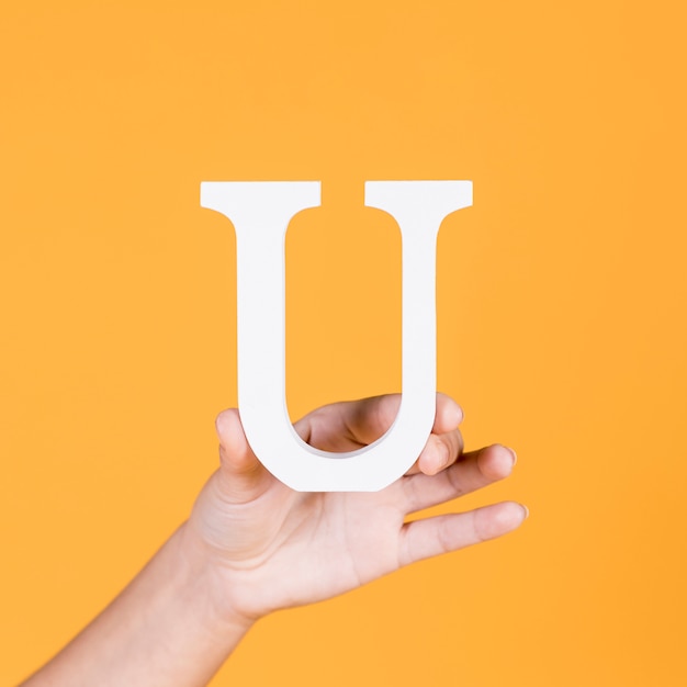 Female hand holding the white uppercase alphabet u over yellow surface