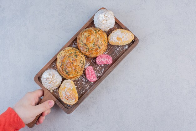 Female hand holding wooden board of sweets. 