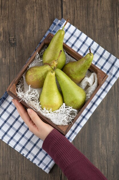 Female hand holding wooden box of delicious ripe pears on wooden background