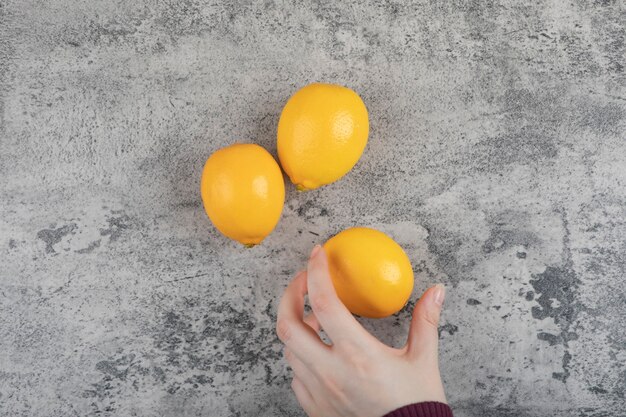 Female hand holding yellow lemon on stone table.