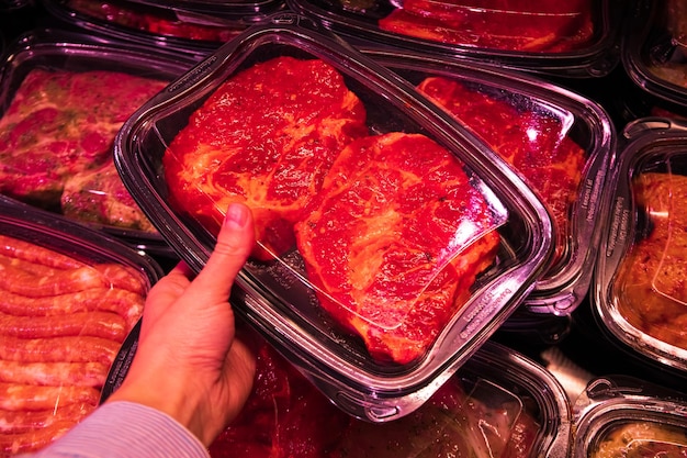 Female hand holds container with meat meat in supermarket