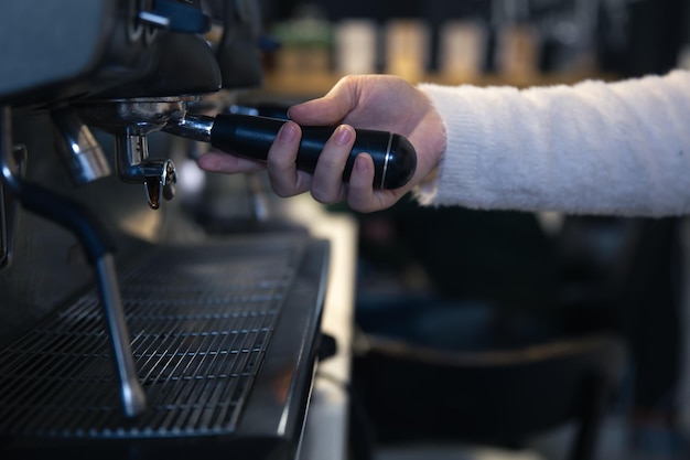 女性の手がプロのコーヒーマシンでホルダーを持っています