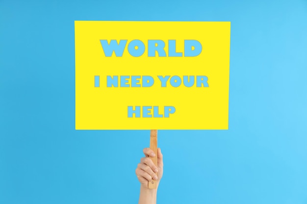 Female hand holds protest sign with text world i need your help on blue background Free Photo