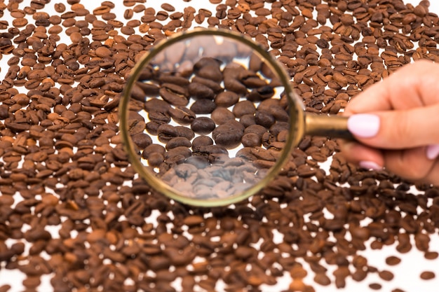 Female hand keepig magnifying glass over the coffee beans