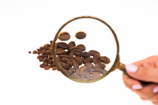 Free photo female hand keeping magnifying glass over the coffee beans